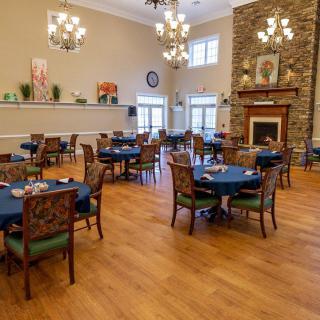 An elegant dining room with multiple round tables, chandeliers, and a fireplace.