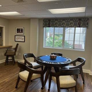 A cozy room with a round table and chairs, brightened by natural light from a large window.