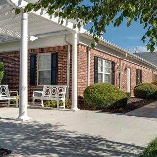 A brick building with a covered porch and benches, surrounded by well-maintained shrubbery.