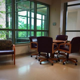 A cozy waiting area featuring comfortable chairs and a table, illuminated by natural light from large windows.