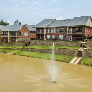 A view of residential apartments with a central pond featuring a fountain.
