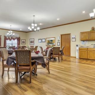A spacious dining room with wooden floors, elegant chandeliers, and multiple dining tables and chairs.