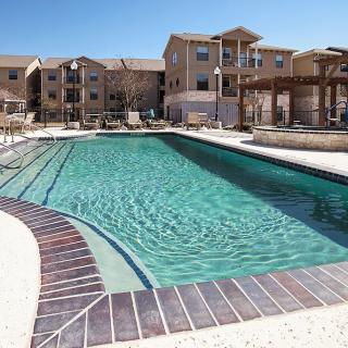 A tranquil swimming pool in an apartment complex under a clear blue sky.