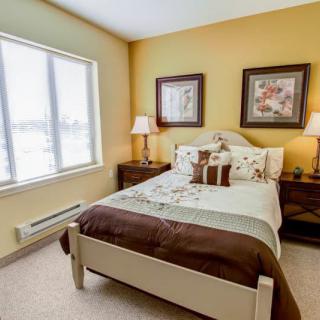 A cozy bedroom with a neatly made bed, flanked by lamps and artwork on the walls.