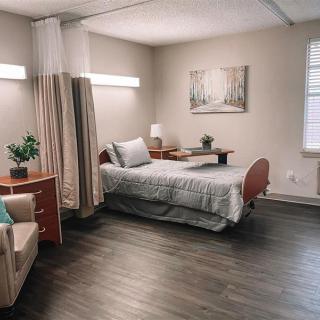 A clean and modern bedroom with minimalist decor, featuring a hospital bed, nightstand, and comfortable seating.