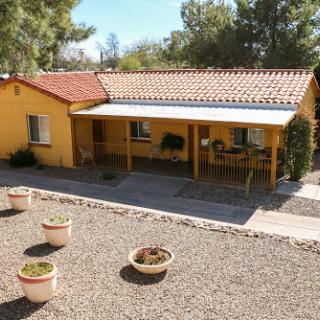 A charming yellow house with a spacious patio surrounded by gravel and potted plants.