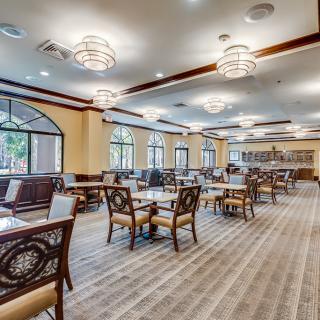 An elegant dining room with arranged tables and chairs, featuring large windows and stylish lighting.