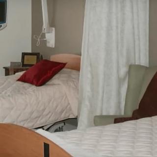 A hospital room with two beds separated by a curtain, featuring pillows on each bed.