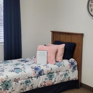 A cozy bedroom featuring a single bed with floral bedding, complemented by pillows and a wall clock.