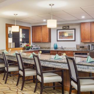 A modern kitchen and dining area featuring a long countertop with bar stools and overhead pendant lights.