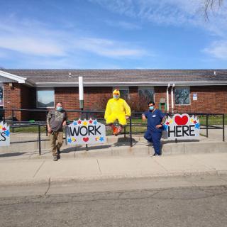 A group of people in various costumes and uniforms stand outside a school building with signs celebrating healthcare workers.