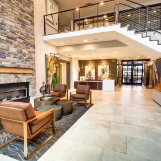 A modern lobby featuring a cozy seating area, fireplace, and reception desk, with an upper-level view accessible via stylish stairs.
