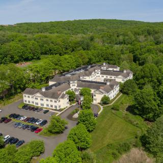 Aerial view of a large building surrounded by lush greenery and parking space.