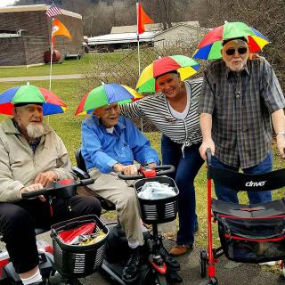A cheerful group of elderly individuals enjoy a day outdoors, wearing colorful umbrella hats and using mobility scooters.