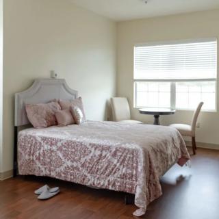 A cozy bedroom with a neatly made bed and natural light streaming through the window.