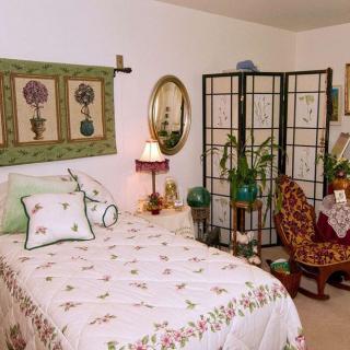 A cozy bedroom with floral-themed decor and a vintage aesthetic, featuring a bed, decorative screen, and various plants.
