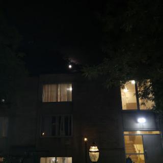 A serene night scene featuring a building illuminated by warm lights and the moon shining in the sky.