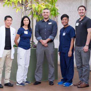 A group of five people standing together outside, dressed in both casual and professional attire.
