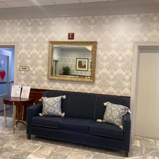 A cozy waiting area featuring a navy blue sofa with decorative pillows, a stylish mirror, and elegant wallpaper.
