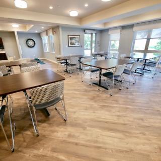A modern dining area with tables and chairs, featuring wood flooring and ample natural light.