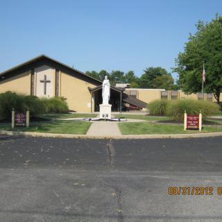 A church with a statue in front, surrounded by greenery.