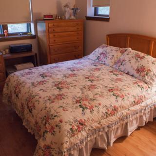 A cozy bedroom featuring a bed with floral bedding, a dresser, and a nightstand.