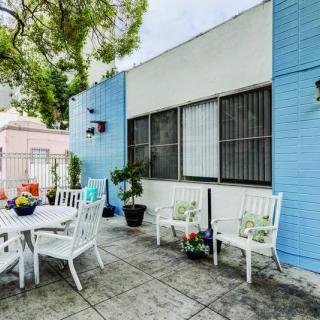 A cozy outdoor patio area featuring a table and chairs surrounded by lush plants against a colorful building backdrop.