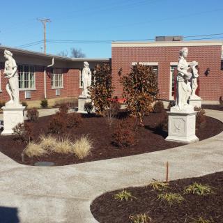 A courtyard garden with statues and a brick building in the background.