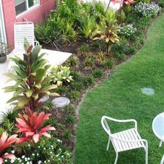 A well-maintained garden featuring vibrant plants and flowers, with a grassy area and patio furniture.