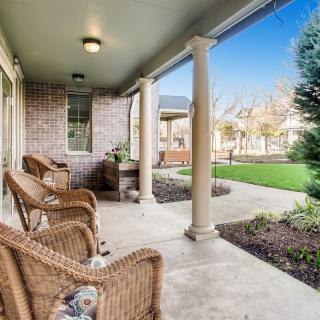 A cozy porch with wicker chairs and decorative columns overlooking a well-maintained garden.