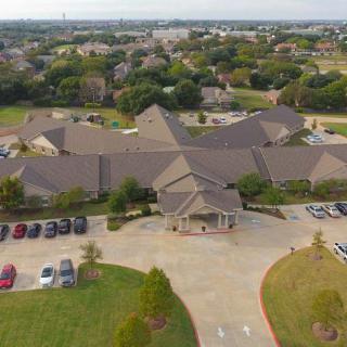 Aerial view of a large building complex surrounded by a parking lot and green landscape in a suburban area.