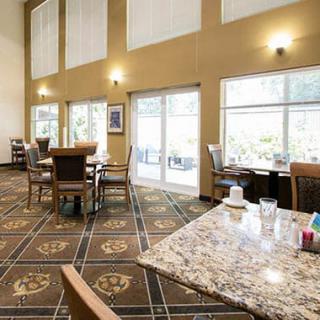 A well-lit dining area with tables and chairs, featuring large windows and patterned carpeting.