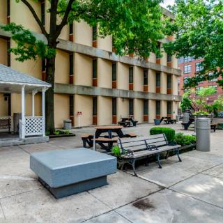 A peaceful urban courtyard with benches and trees, surrounded by a multi-story building.