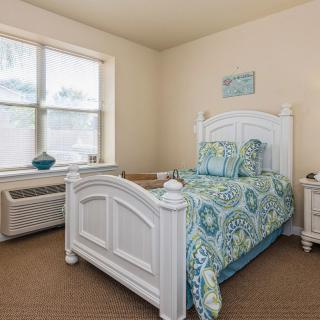 A cozy bedroom with a single bed featuring patterned bedding, a window with ample light, and a nightstand.