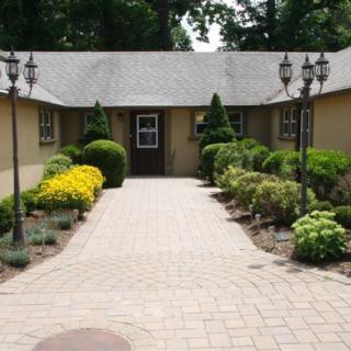 A landscaped pathway leading to a house, flanked by shrubs and flowers.