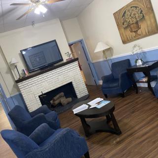 A cozy living room with blue chairs, a fireplace, and a television mounted above.