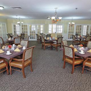 A spacious dining room with neatly arranged tables and chairs, featuring elegant chandeliers and a carpeted floor.