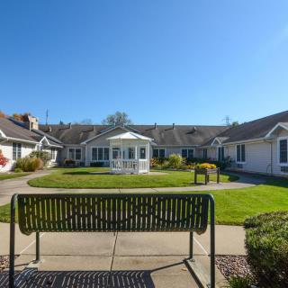 A sunny day in a serene garden with a bench facing a house.