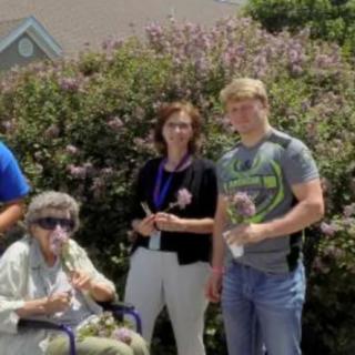 A group of people standing outdoors in a garden, with one person in a wheelchair holding flowers.