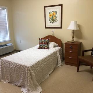 A simple and cozy single bedroom with a nightstand, lamp, and artwork on the wall.