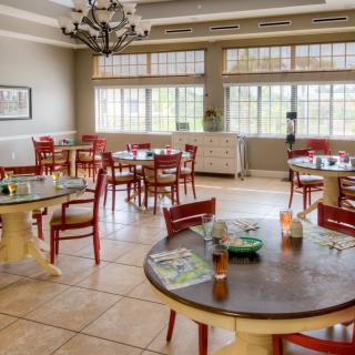 A well-lit dining area with wooden tables and red chairs arranged neatly.