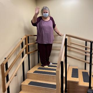 A person standing on stairs, waving while wearing a mask.