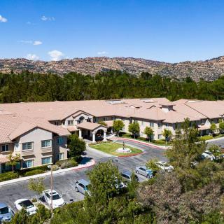 Aerial view of a large building with a parking lot surrounded by trees and mountains under a clear blue sky.
