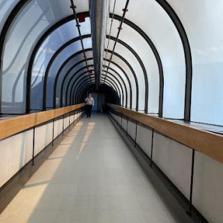 A modern glass corridor with a sleek design, featuring an elongated perspective and natural light.