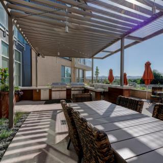 A modern outdoor patio with a pergola and dining area, featuring stylish furniture and surrounded by sunlight.