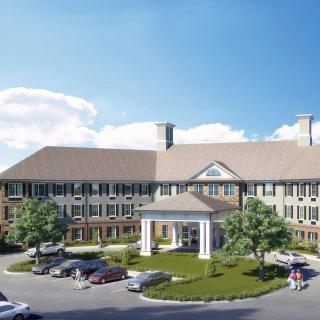 A large, multi-story building with a parking lot and landscaped greenery under a clear blue sky.