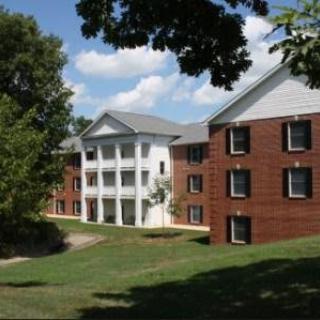 A brick dormitory building on a college campus surrounded by trees under a blue sky.