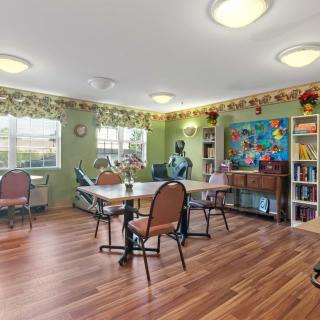 A well-lit community room with tables and chairs, decorated with colorful art and a bookshelf.