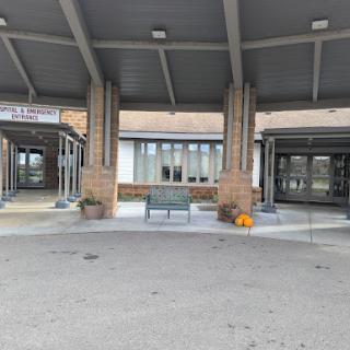 The main entrance of a building, featuring a spacious waiting area with benches and a covered canopy.