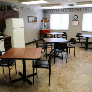 An empty cafeteria with tables, chairs, and a kitchenette area.